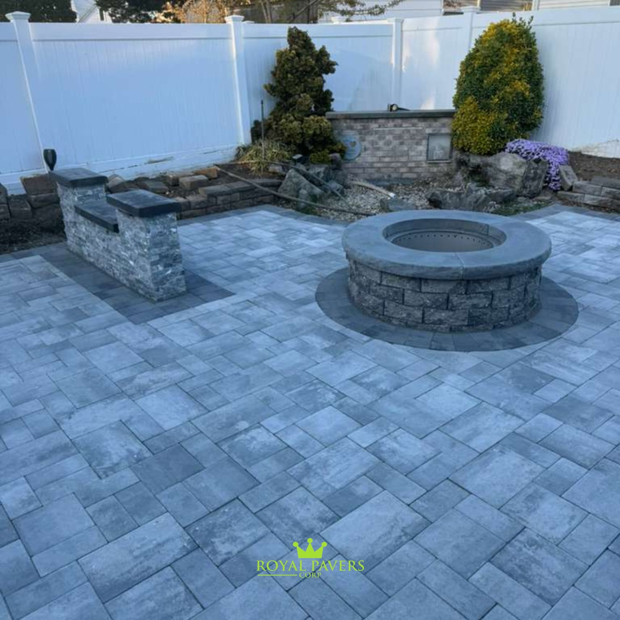 Close-up of a stacked stone fire pit and adjacent sitting wall on a grey paver patio, illustrating professional stone masonry, Long Island by Royal Pavers Corp
