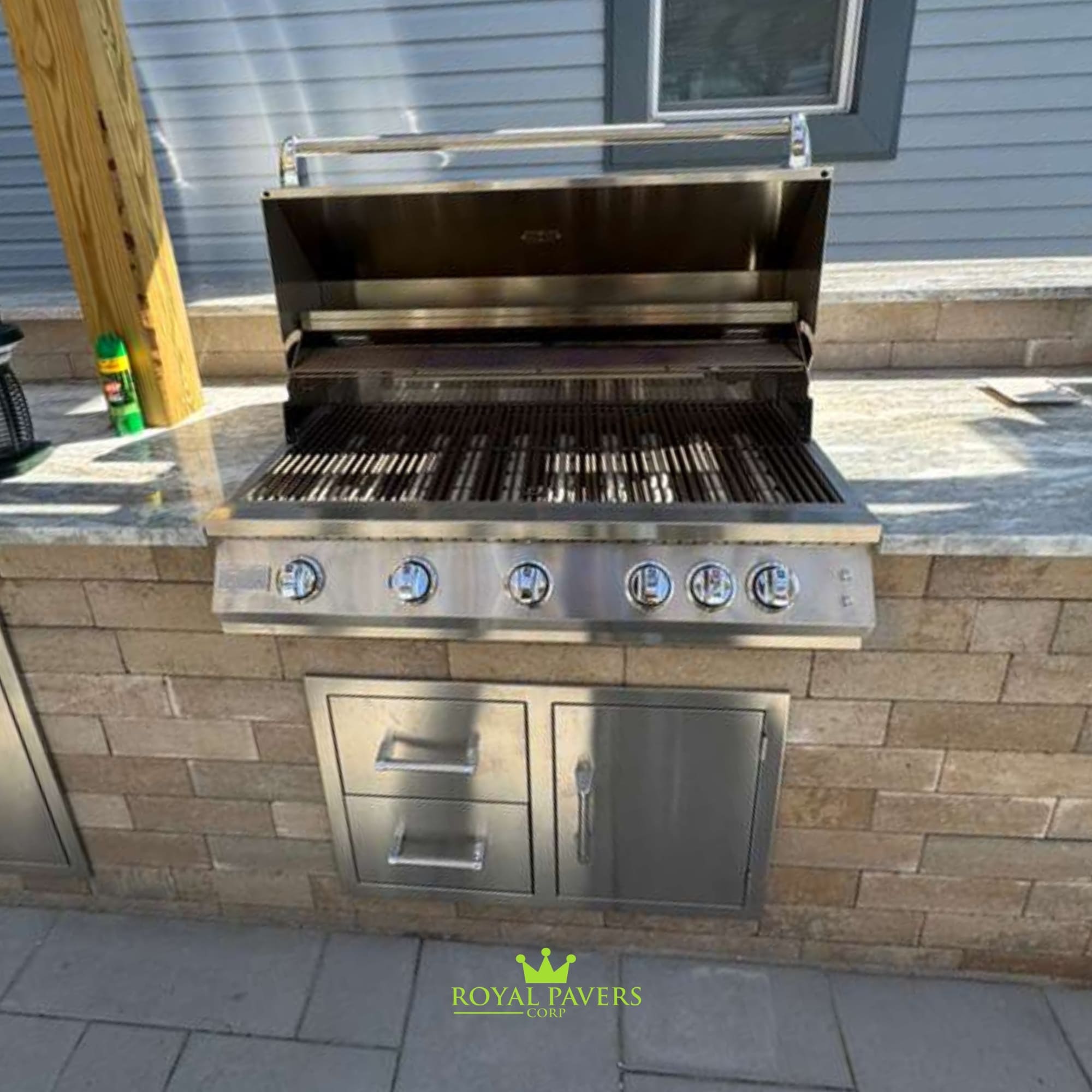 Complete outdoor living renovation with integrated stone fireplace, outdoor kitchen, and expansive paver patio in Long Island by Royal Pavers Corp